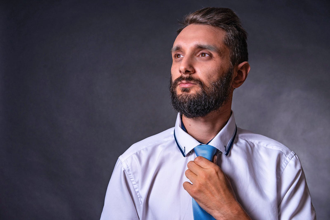 Homme à la barbe soignée et disciplinée ajustant sa cravate en studio
