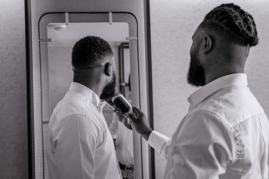 Homme en chemise blanche qui brosse sa barbe devant le miroir, rituel du matin