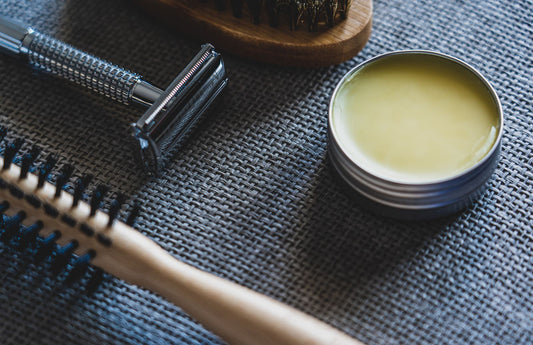 Brosse à barbe en soies naturelles sombres posée à côté d'un rasoir et d'un baume