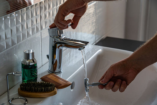 Robinet de salle de bain ouvert avec une brosse à barbe et un peigne posés sur le lavabo